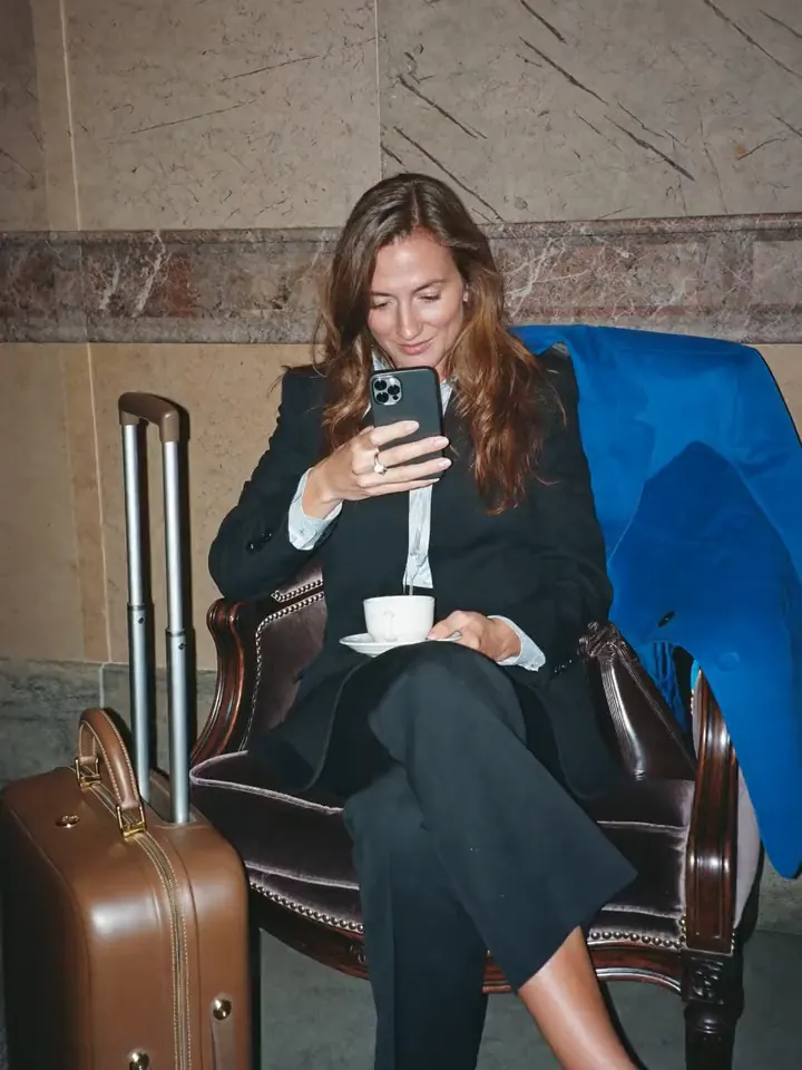 Executive checking her phone over coffee in a hotel lobby, suitcase beside her