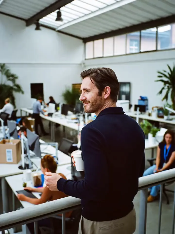 Business owner with a coffee looking out over his team working in a bright open-plan office